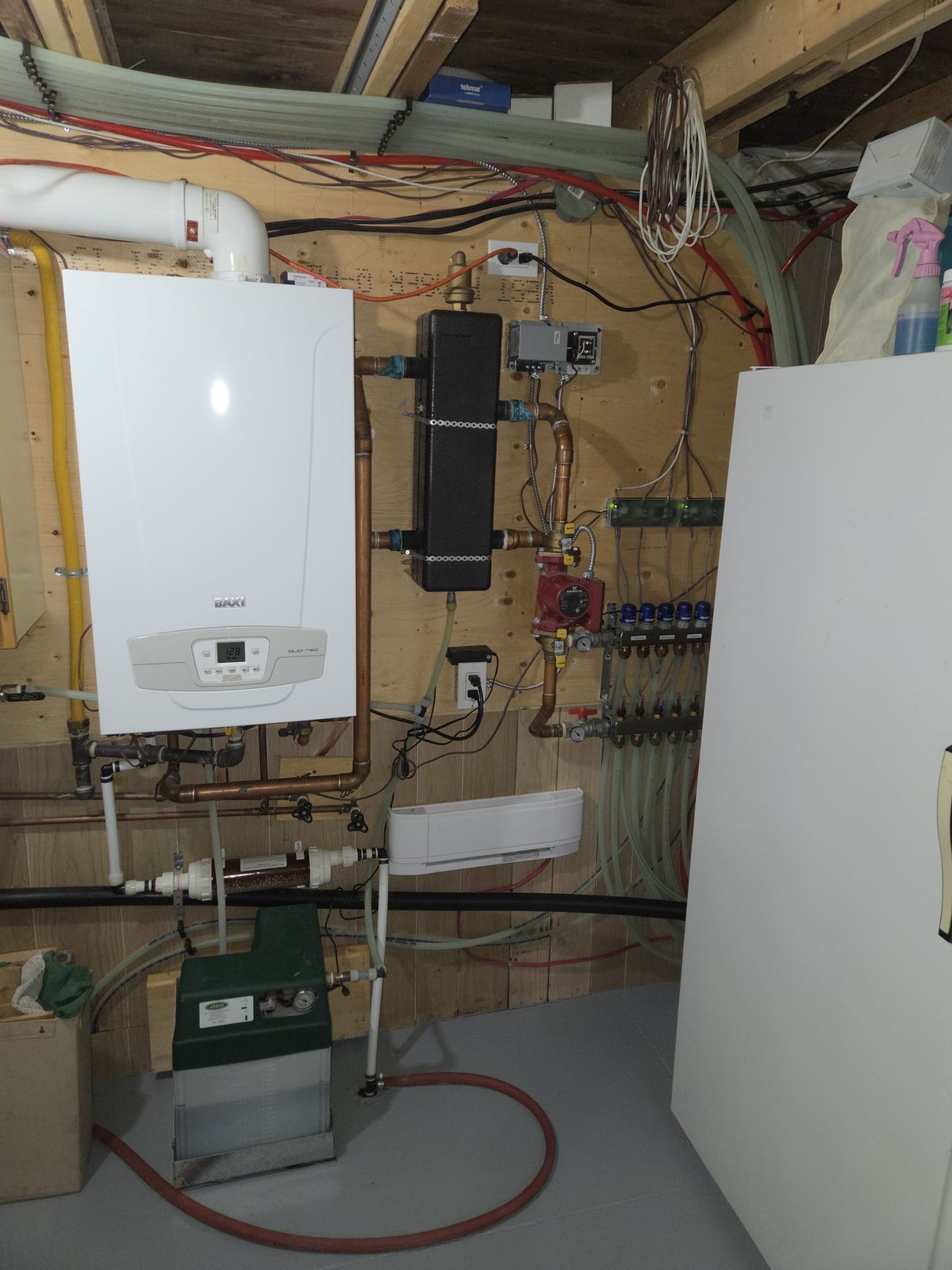 A white wall-hung boiler beside a radiant heating manifold in a basement mechanical room