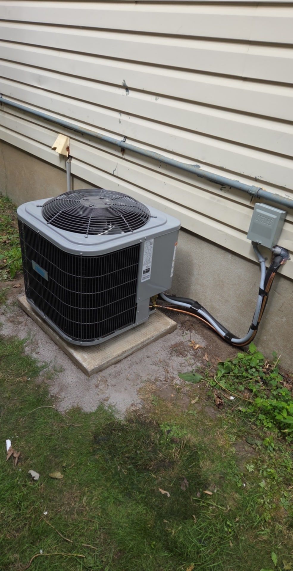 A central air conditioner outdoor unit on a pad beside a house